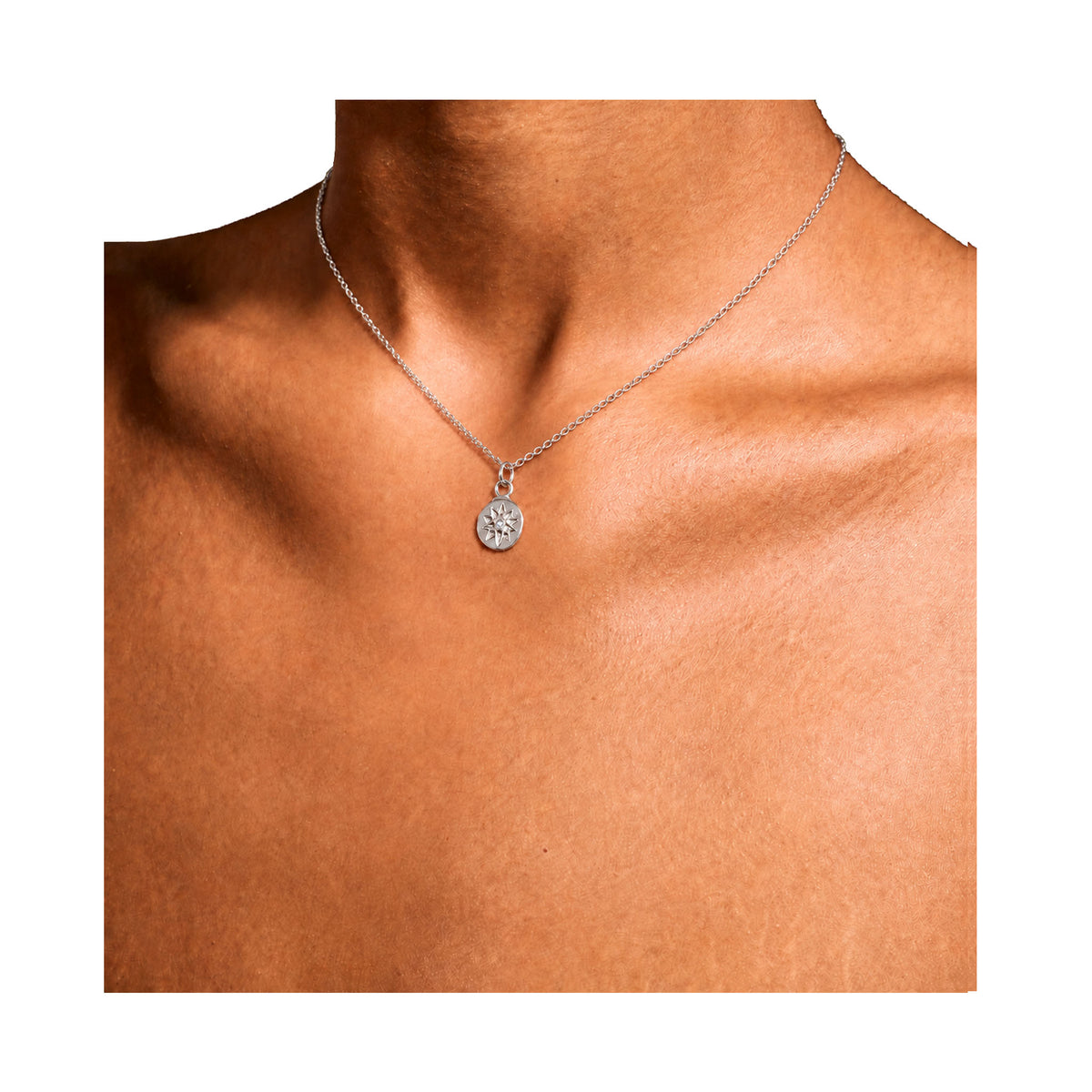 A silver chain necklace with a small round pendant featuring a starburst pattern, shown worn on a model's neck against a plain white background. Handcrafted by Keely Smith Designs on Nantucket